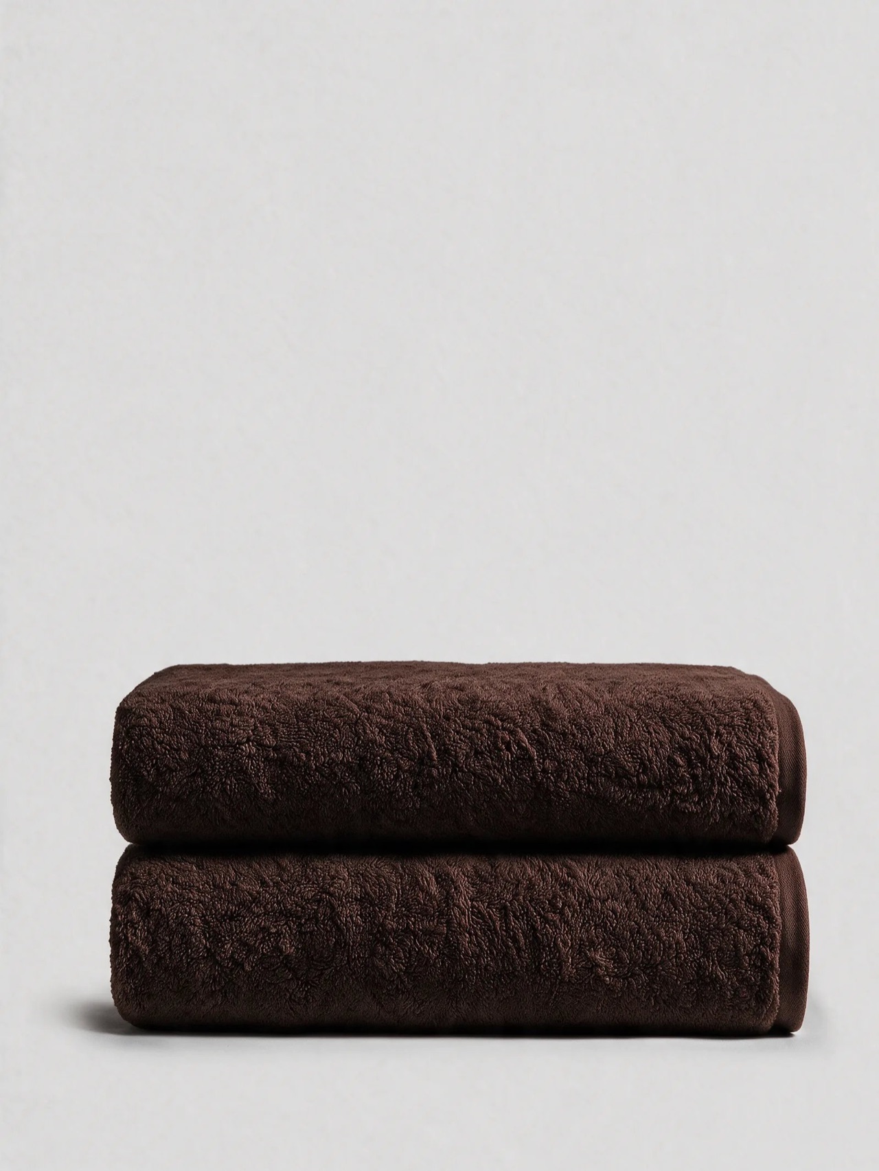 Dark brown Egyptian cotton bath sheets folded in a stack, a solid autumn base for fall and Halloween hand towels
