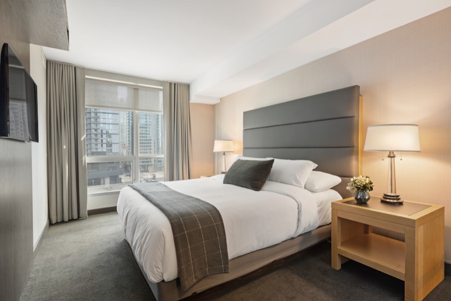 Hotel room bed made with crisp white percale-style sheets, flat and tailored